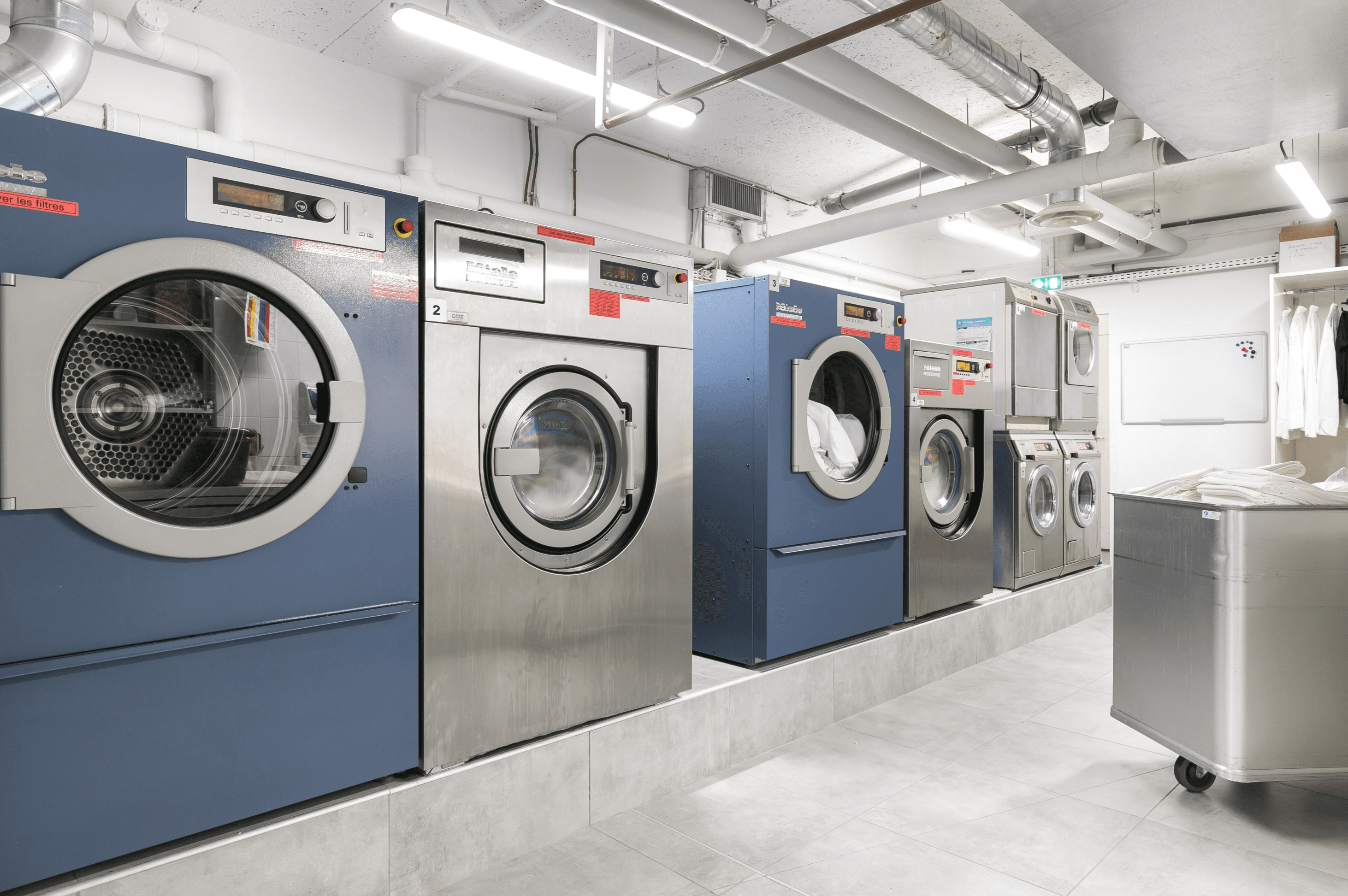 Lave-linge et sèche-linge Miele Professional avec un chariot de linge dans une buanderie