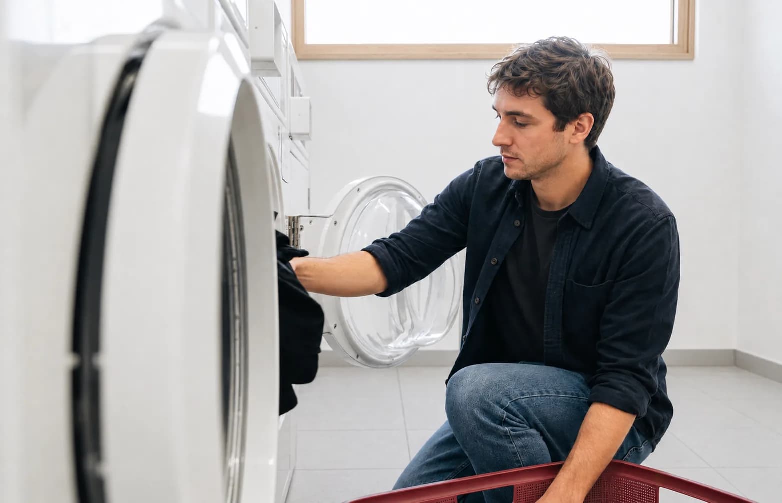Étudiant chargeant son linge dans un lave-linge de la laverie de sa résidence